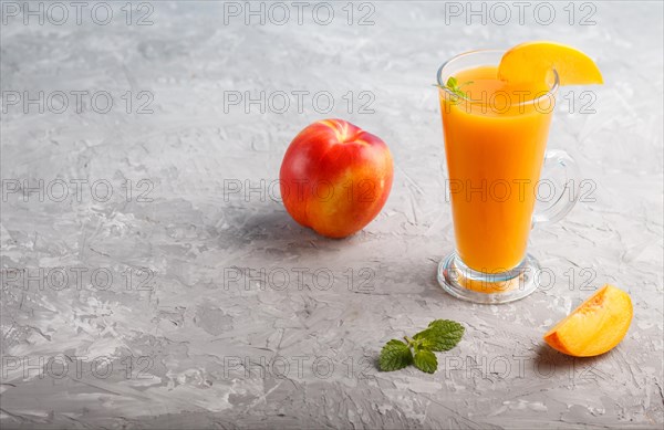 Glass of peach juice on a gray concrete background. Morninig, spring, healthy drink concept. Side view, copy space