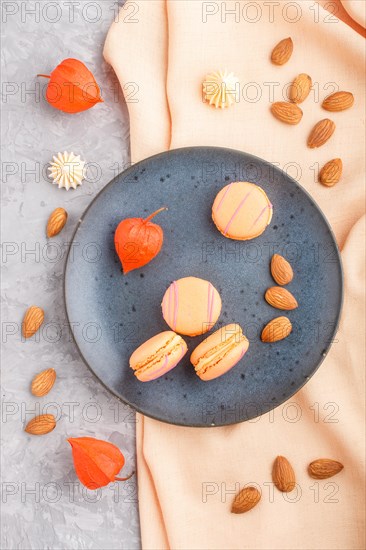 Orange macarons or macaroons cakes on blue ceramic plate on a gray concrete background and orange textile. Flat lay, top view, close up