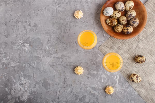 Sweet egg liqueur in glass with quail eggs and meringues on a gray concrete background. Top view, copy space, flat lay