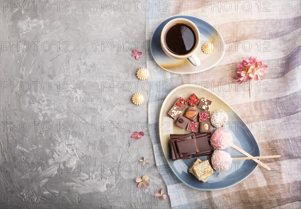 A pieces of homemade chocolate with coconut candies and a cup of coffee on a gray concrete background and blue and brown textile. top view, flat lay, copy space