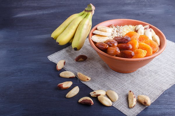 A plate with muesli, banana, dried apricots, dates, Brazil nuts on a black wooden background. close up. copy space