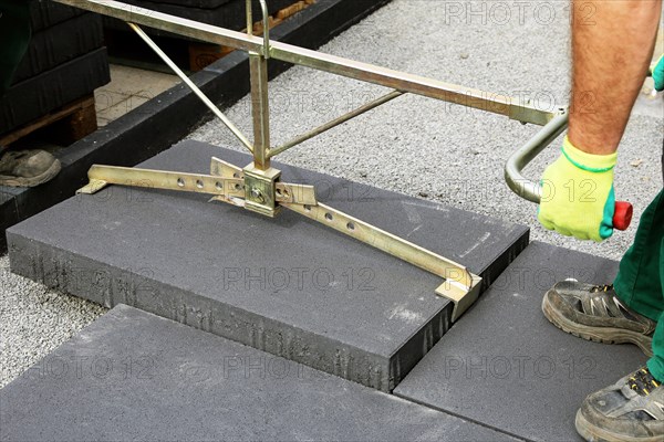 Workers lay heavy paving stones with a stone lifter