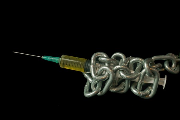 Syringe filled with yellow liquid tied with a chain isolated on black background and copy space, addiction concept