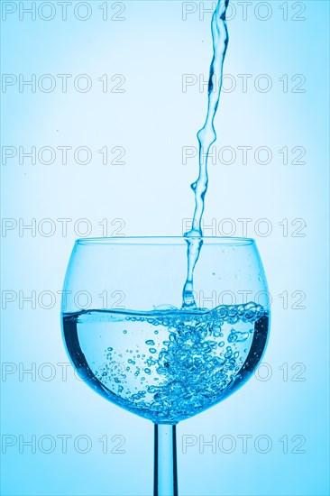 Water is poured into a wine glass on a blue background
