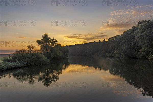 Sunrise in summer on the river ruhr near Iserlohn. The trees are beautifully reflected in the water of the river