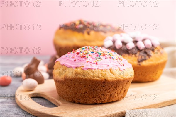 Homemade glazed and decorated easter pies with chocolate eggs and rabbits on a gray and pink background and linen textile. Side view, selective focus, close up
