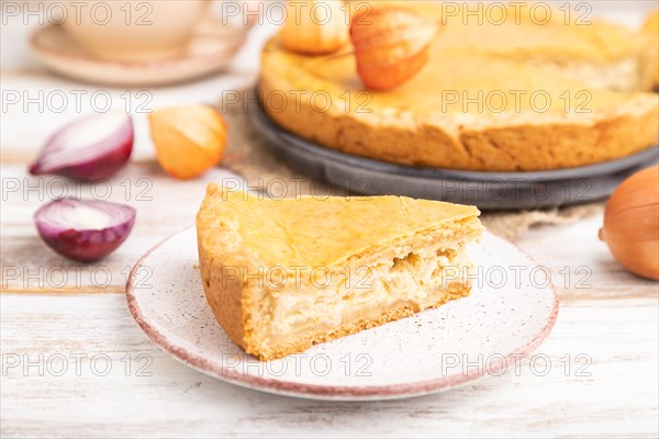 Autumn onion pie and cup of coffee on white wooden background and linen textile. Side view, close up, selective focus