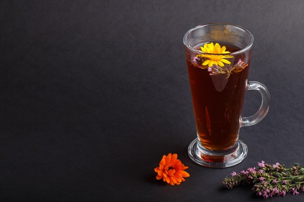 Glass of herbal tea with calendula and hyssop on a black background. Morninig, spring, healthy drink concept. Side view, copy space