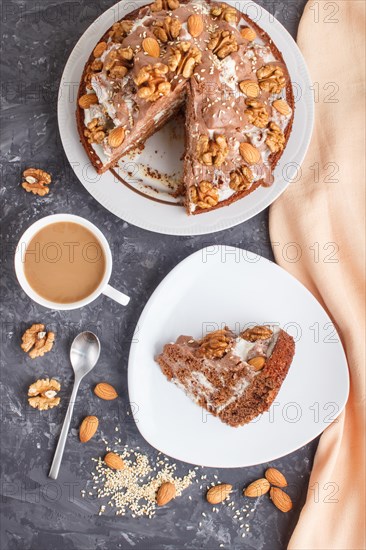 Homemade cake with milk cream, cocoa, almond, hazelnut on a black concrete background with orange textile and a cup of coffee. Top view, flat lay, close up