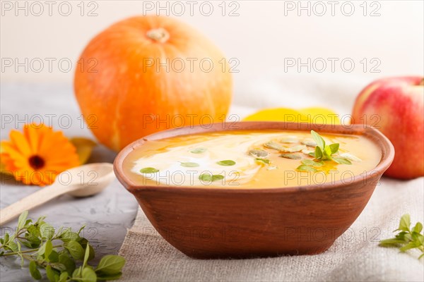 Traditional pumpkin cream soup with seeds in clay bowl on a gray concrete background with linen textile. side view, close up, selective focus