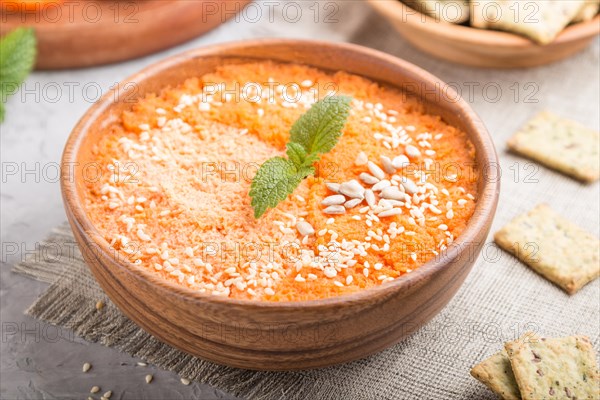 Carrot cream soup with sesame seeds and snacks in wooden bowl on a gray concrete background with linen textile. side view, close up, selective focus