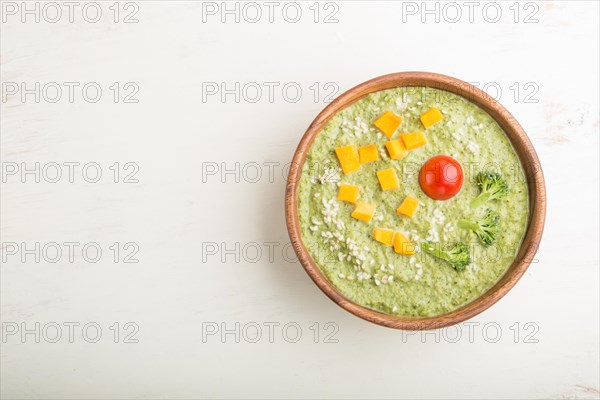 Green broccoli cream soup in wooden bowl on a white wooden background. top view, flat lay, copy space