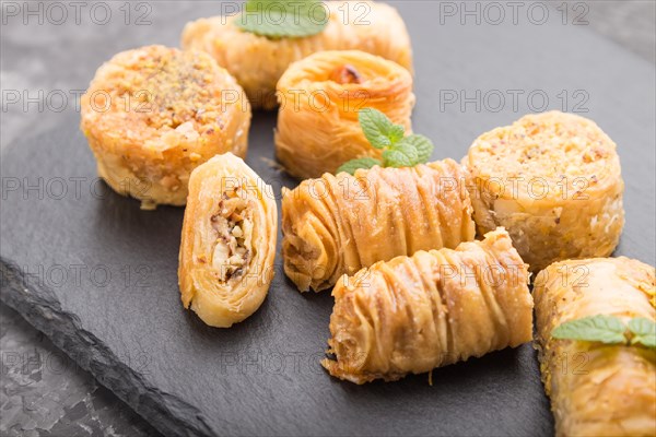 Traditional arabic sweets (kunafa, baklava) on a black slate board on a black concrete background. side view, close up, selective focus