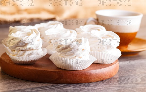 White marshmallows (zephyr) on a round wooden board with cup of coffee on a gray wooden background