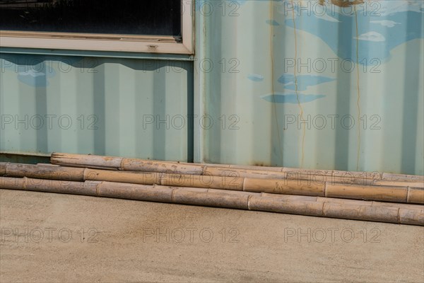 Weathered cracked bamboo poles laying on concrete driveway in front of aluminum building wall in South Korea