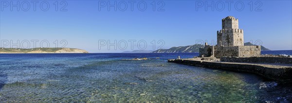 An old stone tower on a coast with crystal clear sea water under a wide blue sky, octagonal medieval tower. Islet of Bourtzi, sea fortress of Methoni, Peloponnese, Greece, Europe