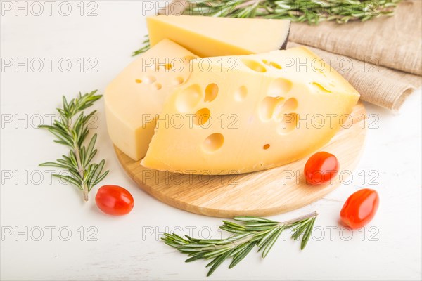 Various types of cheese with rosemary and tomatoes on wooden board on a white wooden background and linen textile. Side view, close up, close up, selective focus