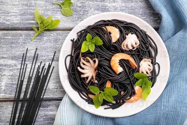 Black cuttlefish ink pasta with shrimps or prawns and small octopuses on gray wooden background and blue textile. Top view, flat lay, close up