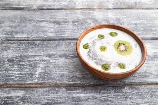 Yogurt with kiwi, gooseberry, chia and almonds in wooden bowl on gray wooden background. side view, copy space, close up