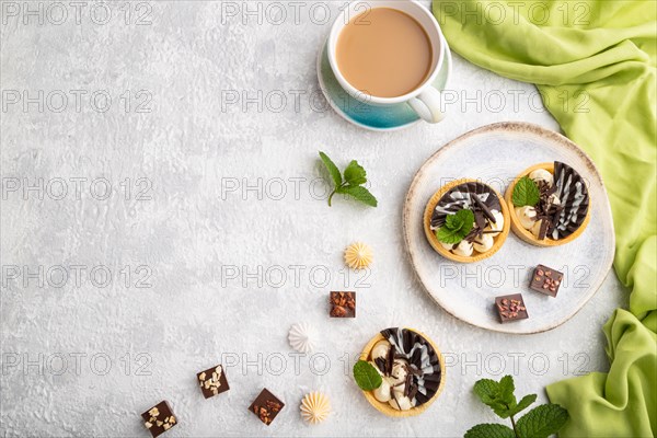 Sweet tartlets with chocolate and cheese cream with cup of coffee on a gray concrete background and green textile. top view, flat lay, copy space