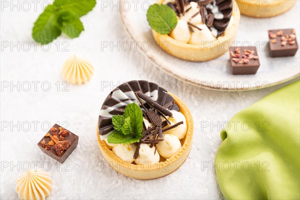 Sweet tartlets with chocolate and cheese cream with cup of coffee on a gray concrete background and green textile. Side view, close up, selective focus