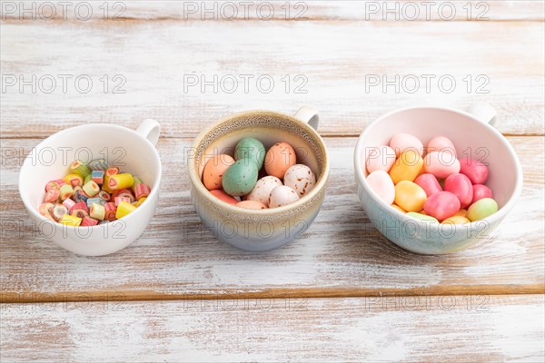 Heap of multicolored caramel candies in cups on white wooden background. copy space, side view, close up