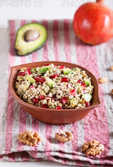 Salad of germinated buckwheat, avocado, walnut and pomegranate seeds in clay plate on white wooden background. Side view, close up, selective focus