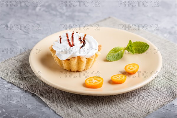 Cake with whipped egg cream on a light brown plate with kumquat slices and mint leaves on a gray concrete background with linen napkin. selective focus, close up. side view