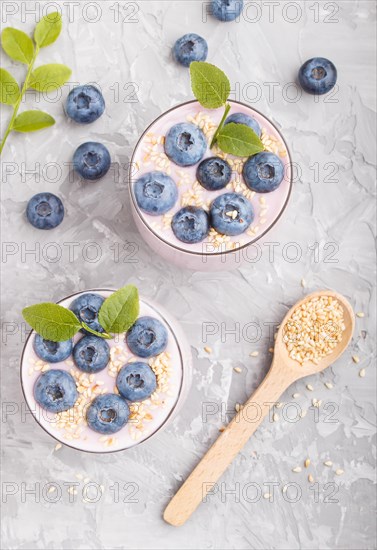 Yoghurt with blueberry and sesame in a glass and wooden spoon on gray concrete background. top view, flat lay, close up