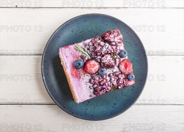 Berry cake with milk cream and blueberry jam on blue ceramic plate on a white wooden background. top view, flat lay, close up