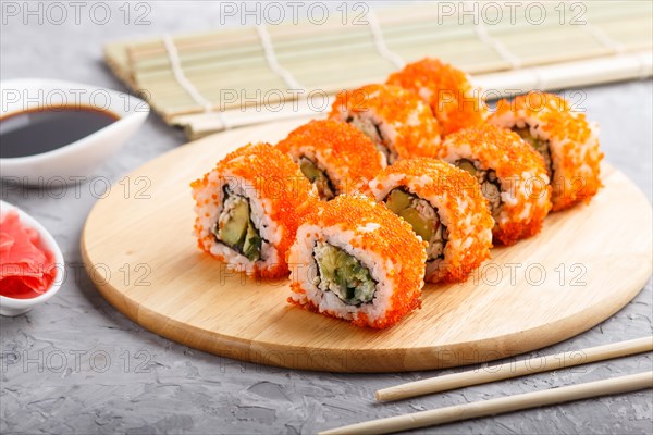 Japanese maki sushi rolls with flying fish roe, chopsticks, soy sauce and marinated ginger on wooden board on a gray concrete background. Side view, close up, selective focus