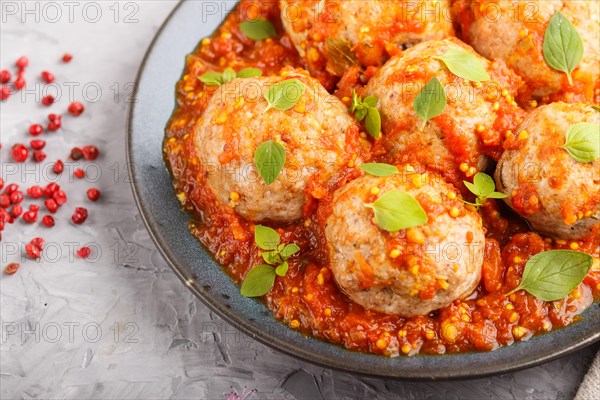 Pork meatballs with tomato sauce, oregano leaves, spices and herbs on blue ceramic plate on a gray concrete background top view, close up, selective focus