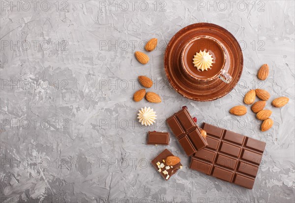 Cup of hot chocolate and pieces of milk chocolate with almonds on a gray concrete background. Flat lay, top view, copy space