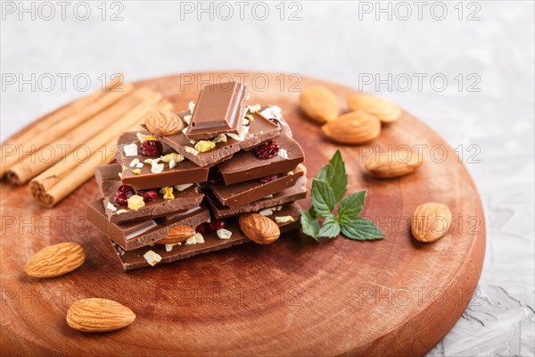 A pieces of milk chocolate with almonds and dried fruits on a brown wooden board on a gray concrete background. side view, close up, selective focus