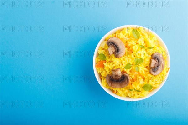 Yellow fried rice with champignons mushrooms, turmeric and oregano in white ceramic bowl on a blue pastel background. Top view, flat lay, copy space