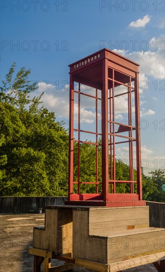 Red wooden telephone booth minus phone and without glass on roof of building on sunny day with blue skies in South Korea