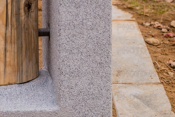 Closeup of bottom of unpainted wooden post held in concrete footing with large threaded bolts in South Korea