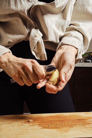 Unrecognizable woman peeling ginger with spoon, close up view