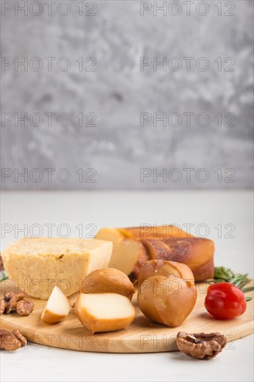Smoked cheese and various types of cheese with rosemary and tomatoes on wooden board on a gray and white background. Side view, copy space, selective focus