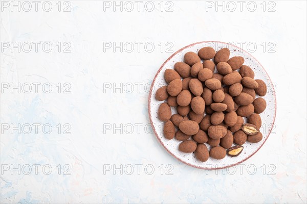 Almond in chocolate dragees on ceramic plate on white concrete background. Top view, copy space, flat lay