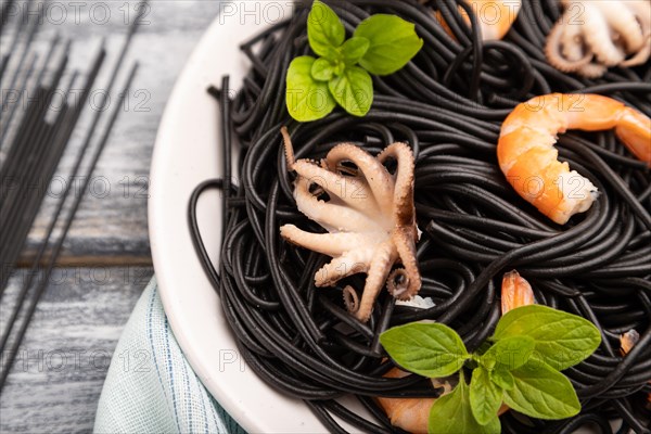 Black cuttlefish ink pasta with shrimps or prawns and small octopuses on gray wooden background and blue textile. Side view, close up, selective focus