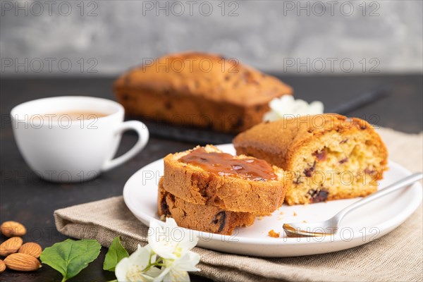 Homemade cake with raisins, almonds, soft caramel and a cup of coffee on a black concrete background and linen textile. Side view, close up, selective focus