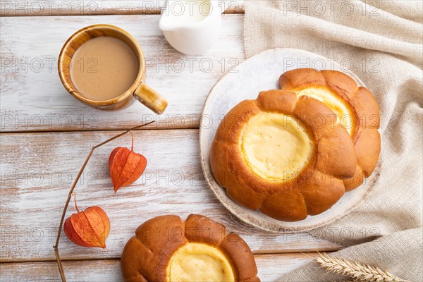 Sour cream bun with cup of coffee on a white wooden background and linen textile. top view, flat lay, close up