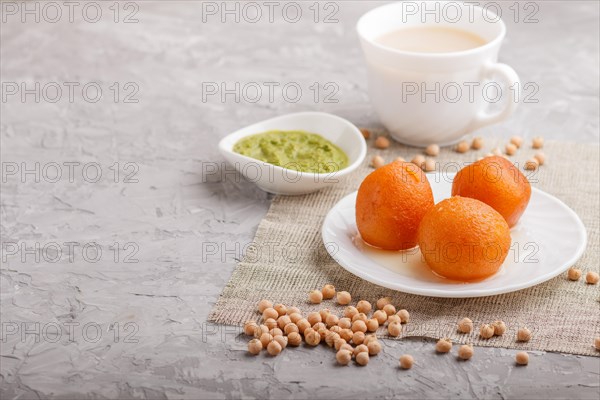 Traditional indian candy gulab jamun in white plate with mint chutney on a gray concrete background. side view, copy space