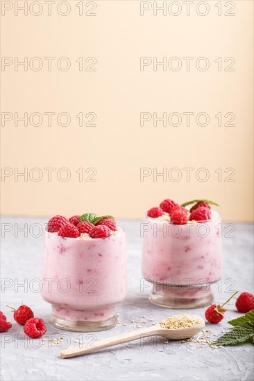 Yoghurt with raspberry and sesame in a glass and wooden spoon on gray and orange background. side view, close up