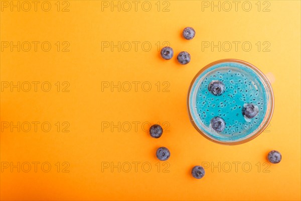 Glass of blueberry blue colored drink with basil seeds on orange background. Morninig, spring, healthy drink concept. Top view, copy space, flat lay
