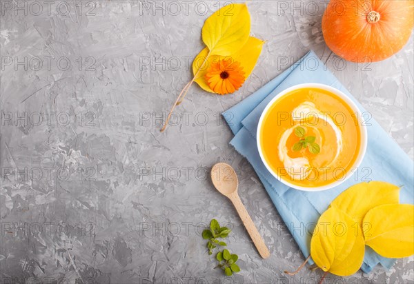 Traditional pumpkin cream soup with in white bowl on a gray concrete background with blue napkin. top view, flat lay, copy space