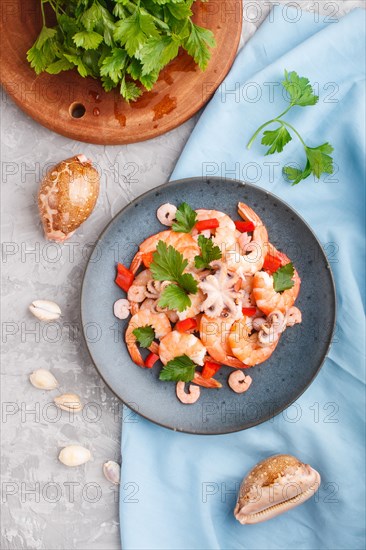 Boiled shrimps or prawns and small octopuses with herbs on a blue ceramic plate on a gray concrete background and blue textile. Top view, flat lay, close up