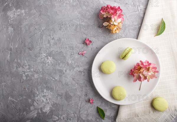 Green macarons or macaroons cakes on white ceramic plate on a gray concrete background and linen textile. Flat lay, top view, copy space