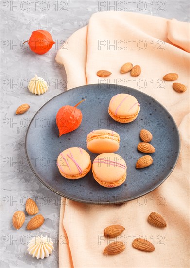 Orange macarons or macaroons cakes on blue ceramic plate on a gray concrete background and orange textile. side view, close up